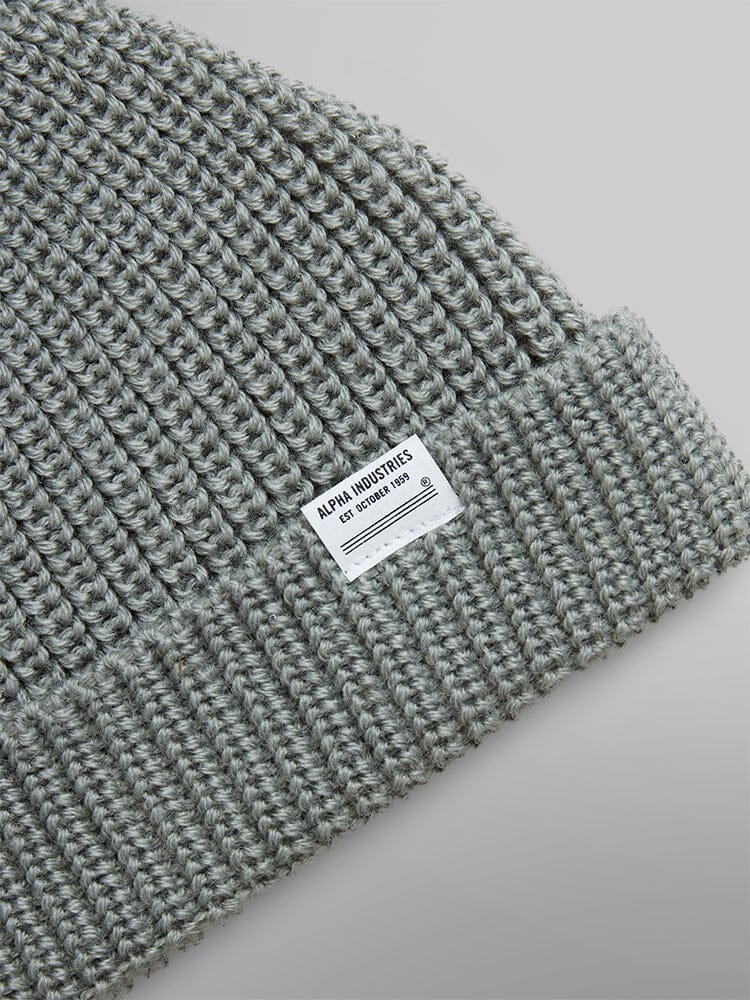 The Essential Watch Cap by Alpha Industries, a gray wool-blend knit beanie, features a white label on the fold and is styled like a watch cap.