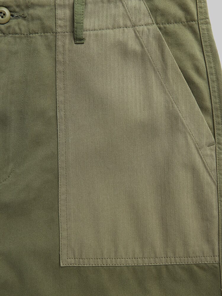Alpha Industries Fatigue Pant in olive green cotton with large front utility pocket, visible stitching, and button near waistband.