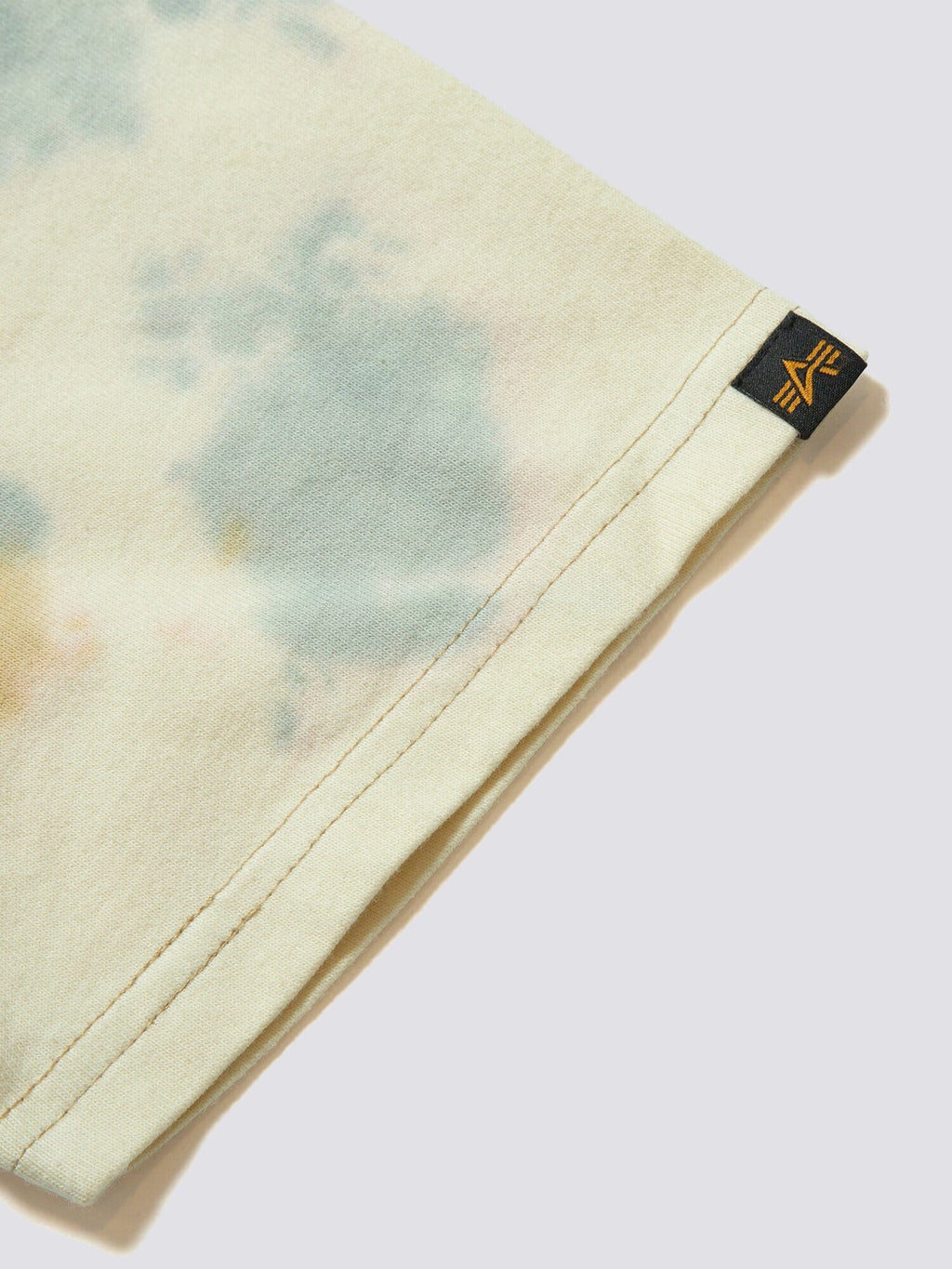Gramicci X Alpha Cotton Camo Tie Dye Tee by Alpha Industries, light tie-dye cotton fabric, small black and yellow Gramicci logo tag at hem.