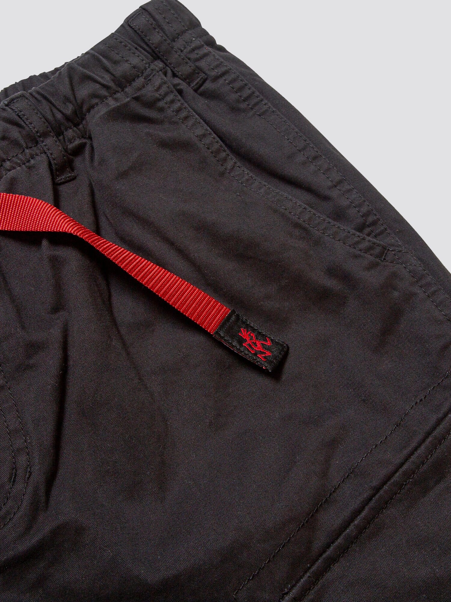 Gramicci X Alpha Jungle Cargo Short by Alpha Industries in black, elastic waistband, side pocket, cargo pockets, red adjustable belt with black patch and small red graphic.