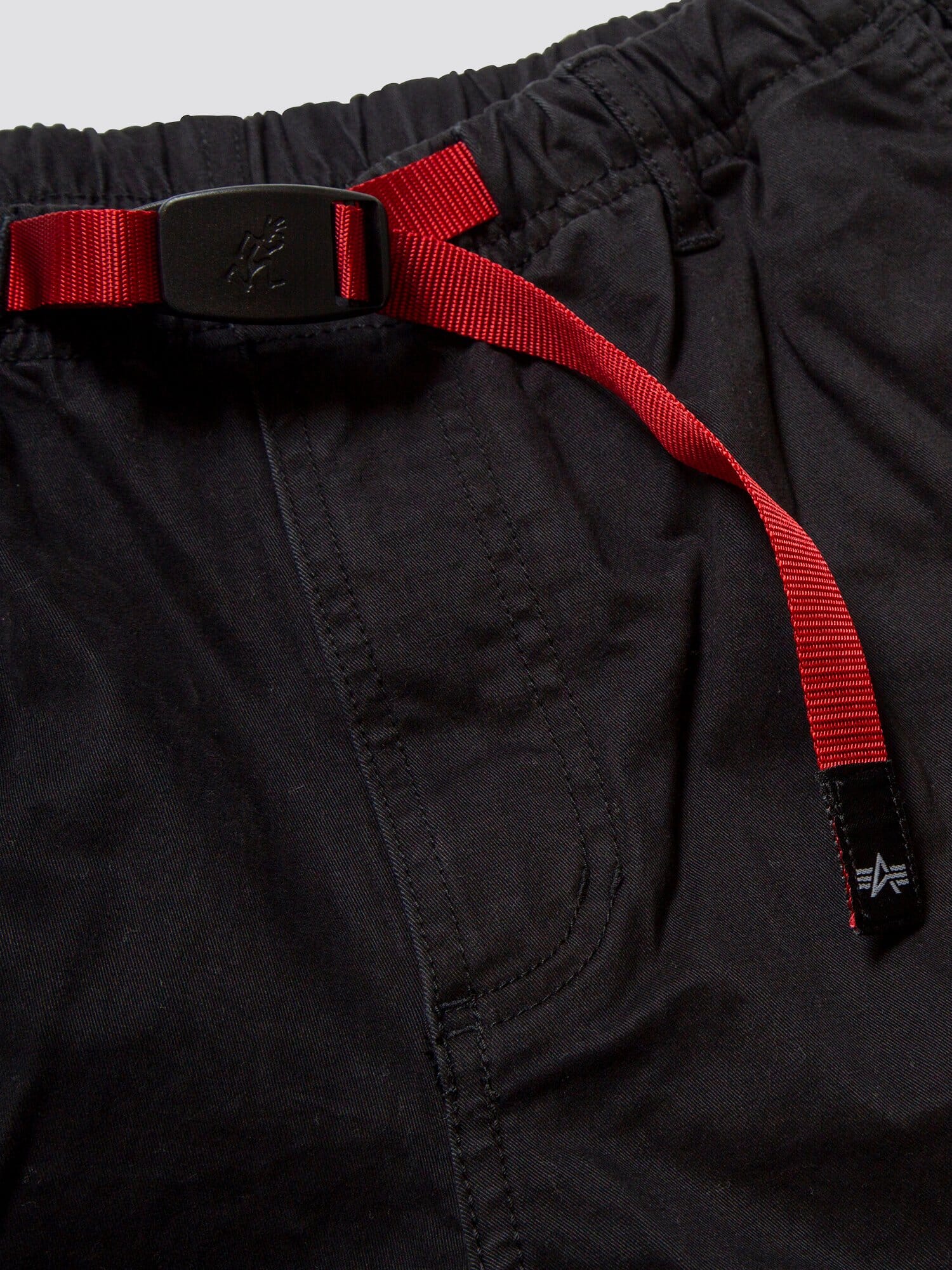 Gramicci X Alpha Jungle Cargo Short by Alpha Industries, black stretch ripstop fabric, elastic waistband, red adjustable belt with plastic buckle, visible stitching, front pocket.