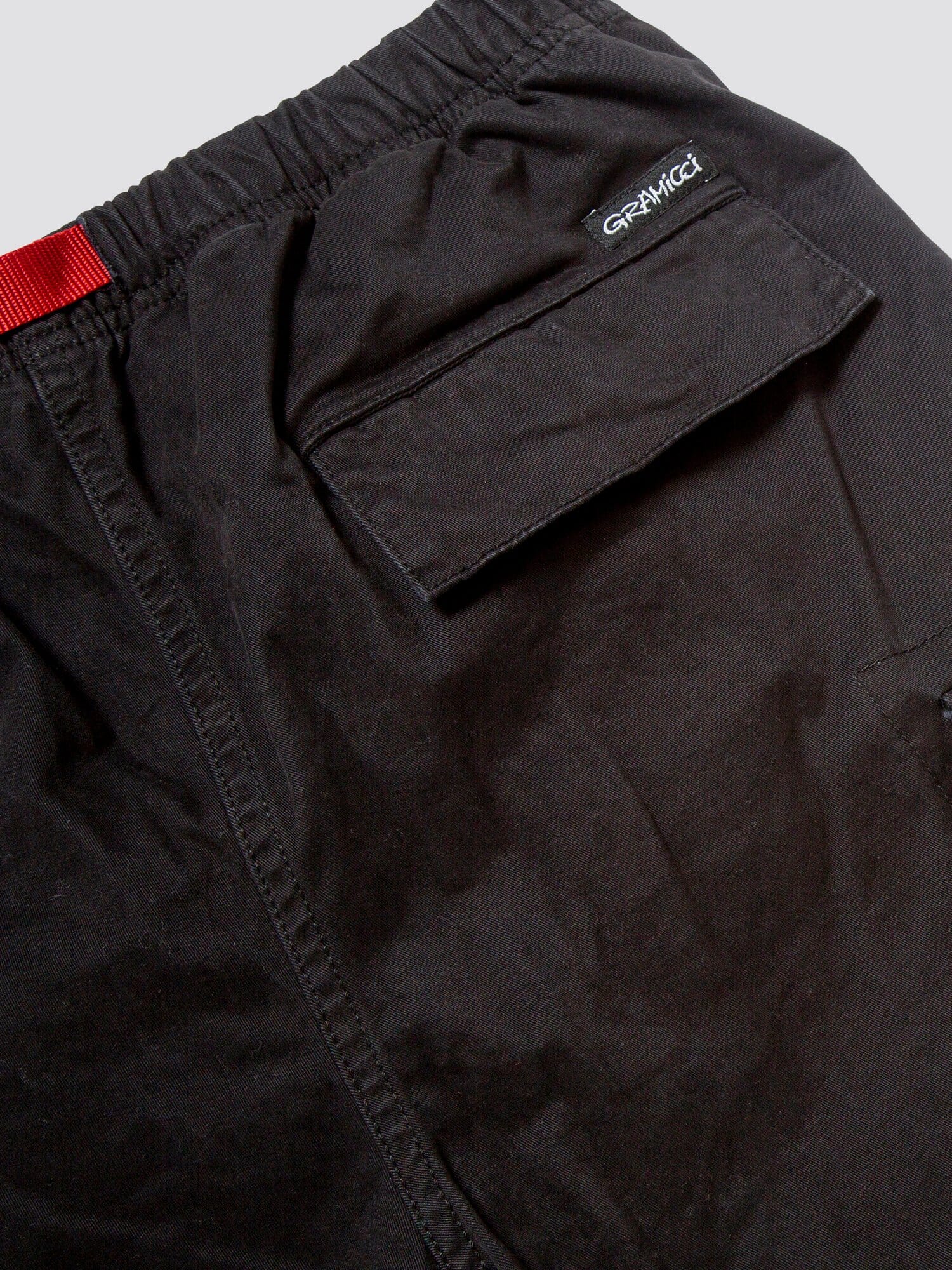 Gramicci X Alpha Jungle Cargo Short by Alpha Industries, black stretch ripstop fabric, flap pocket, visible stitching, red waistband detail, Gramicci logo embroidered above pocket.