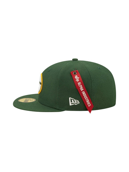Side view of the Green Bay Packers x Alpha x New Era 59FIFTY Fitted Cap in green, featuring an embroidered team logo and a red Alpha Industries tag on the side.
