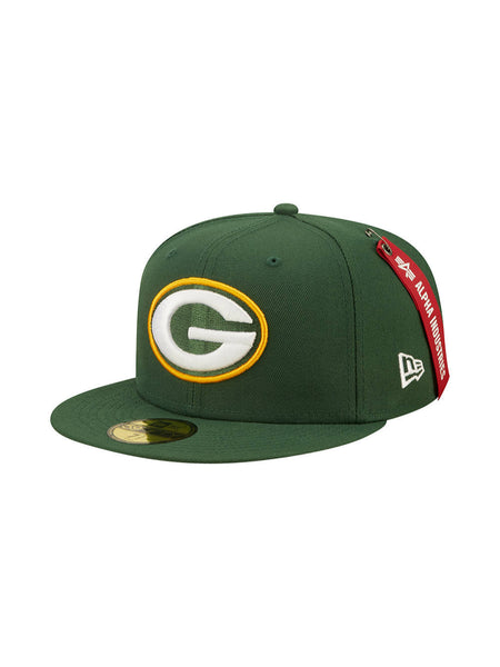 The Green Bay Packers X Alpha X New Era 59Fifty Fitted Cap from Alpha Industries features a prominently embroidered team logo with a bold yellow "G" on the front, reflecting the team colors. This dark green cap includes a striking red tag on the side and a stylish flat brim, showcasing Alpha Industries' distinctive flair.