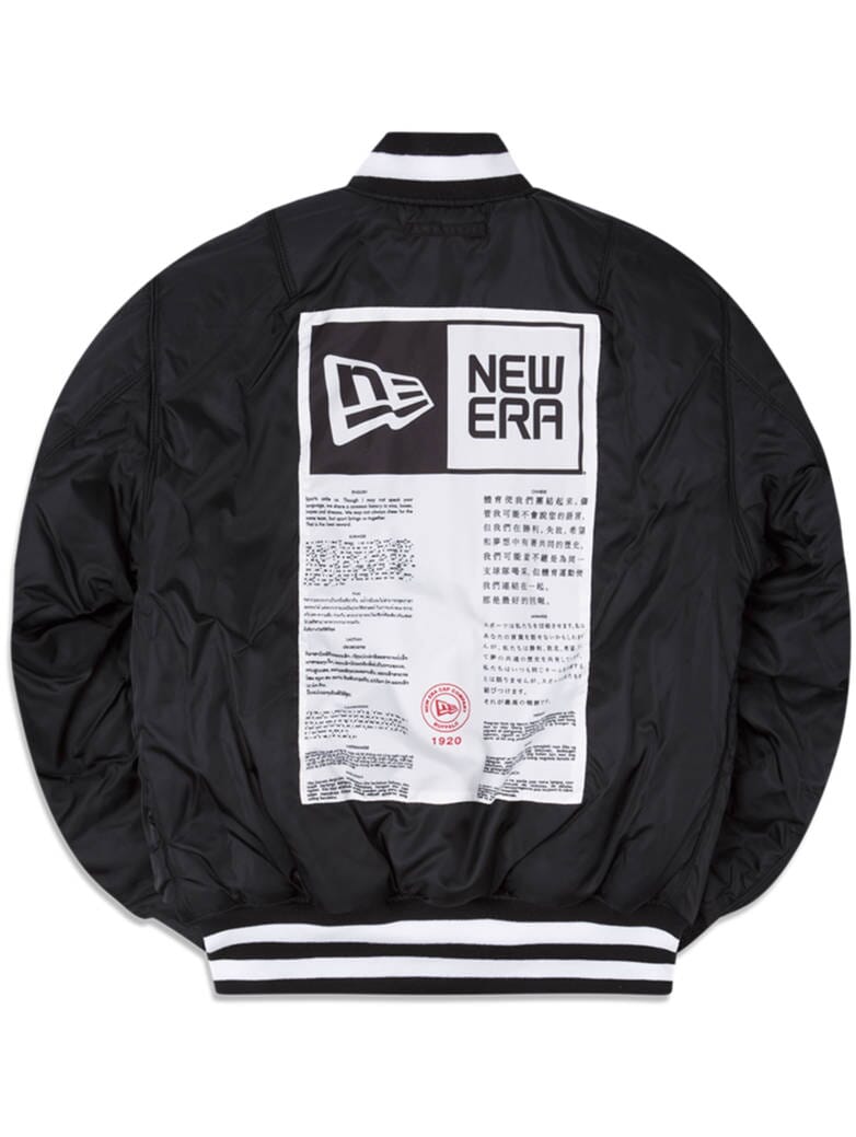 The Green Bay Packers x Alpha Industries x New Era MA-1 Bomber Jacket is a stylish black piece featuring a prominent white label design on the back, adorned with the New Era logo and multilingual text. It also sports white striped ribbed cuffs, collar, and hem for a polished finish.