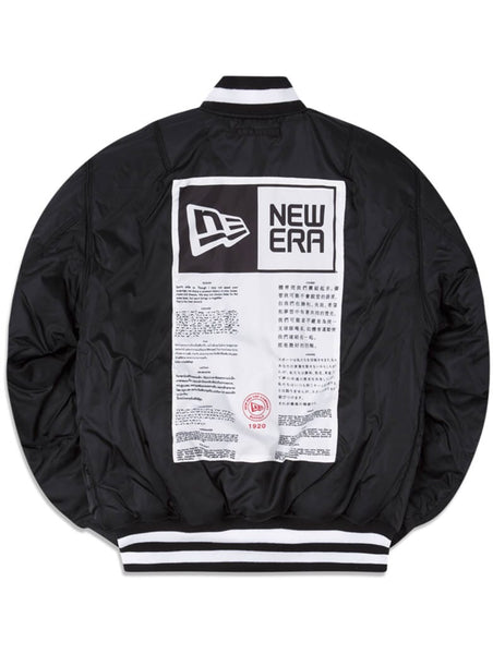 The Green Bay Packers x Alpha Industries x New Era MA-1 Bomber Jacket is a stylish black piece featuring a prominent white label design on the back, adorned with the New Era logo and multilingual text. It also sports white striped ribbed cuffs, collar, and hem for a polished finish.