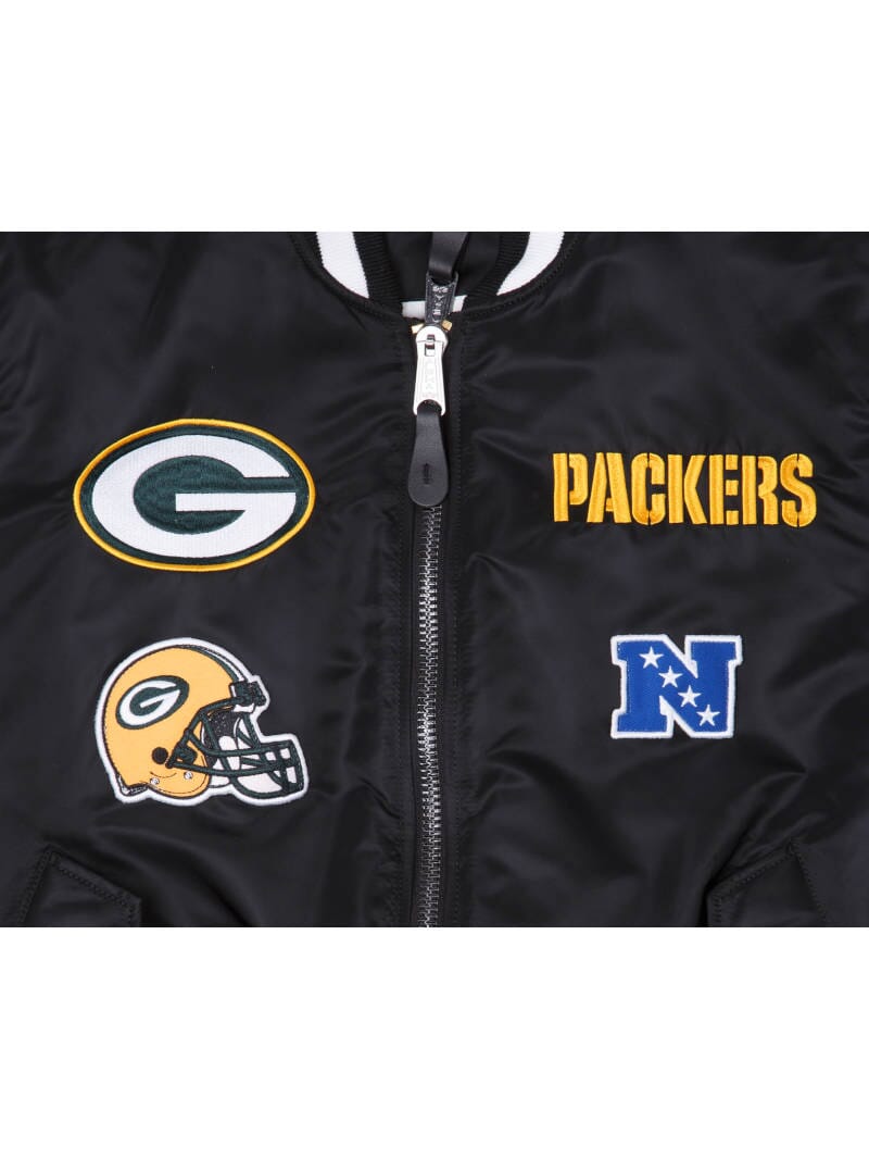 The Green Bay Packers X Alpha X New Era MA-1 Bomber Jacket from Alpha Industries in collaboration with New Era features a reversible design adorned with Green Bay Packers logos, including the iconic G emblem, Packers text, a helmet design, and an NFC logo.