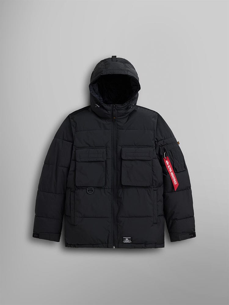 The Hooded Puffer Jacket by Alpha Industries, Inc. is crafted from matte nylon in black. It features an insulated hood, front zipper, two large chest pockets, and a distinctive red tag hanging from the left sleeve.