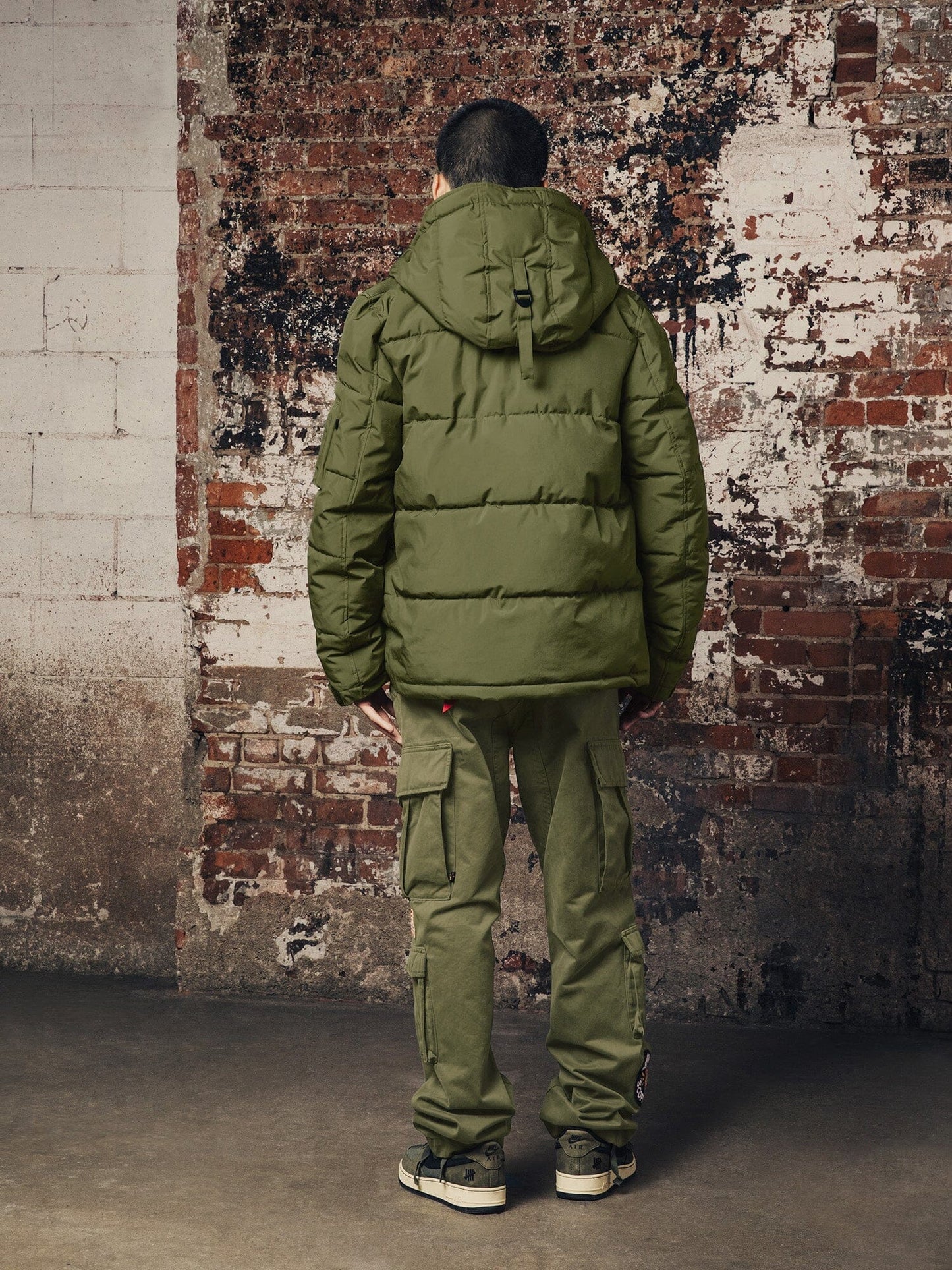 An individual wearing a Hooded Puffer Jacket by Alpha Industries, Inc. and cargo pants is standing.