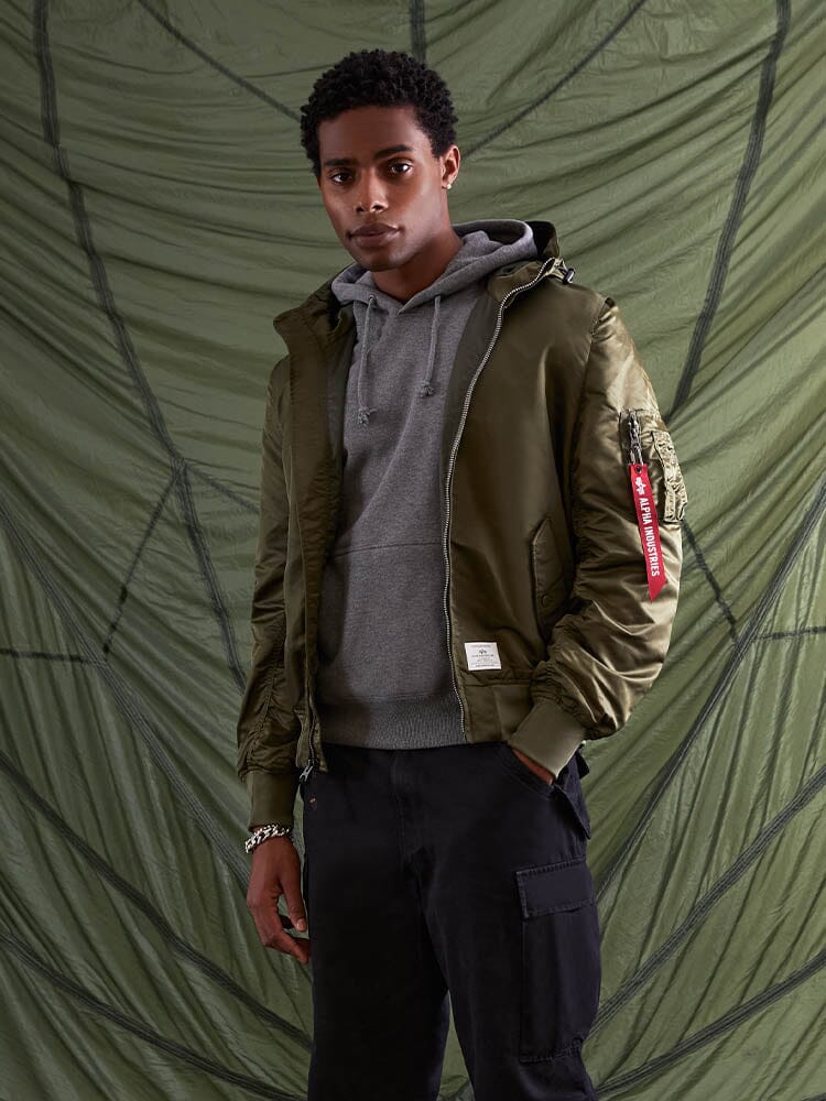 Someone wearing the Alpha Industries, Inc. L-2B Hooded Gen II Bomber Jacket in green, paired with a gray hoodie.