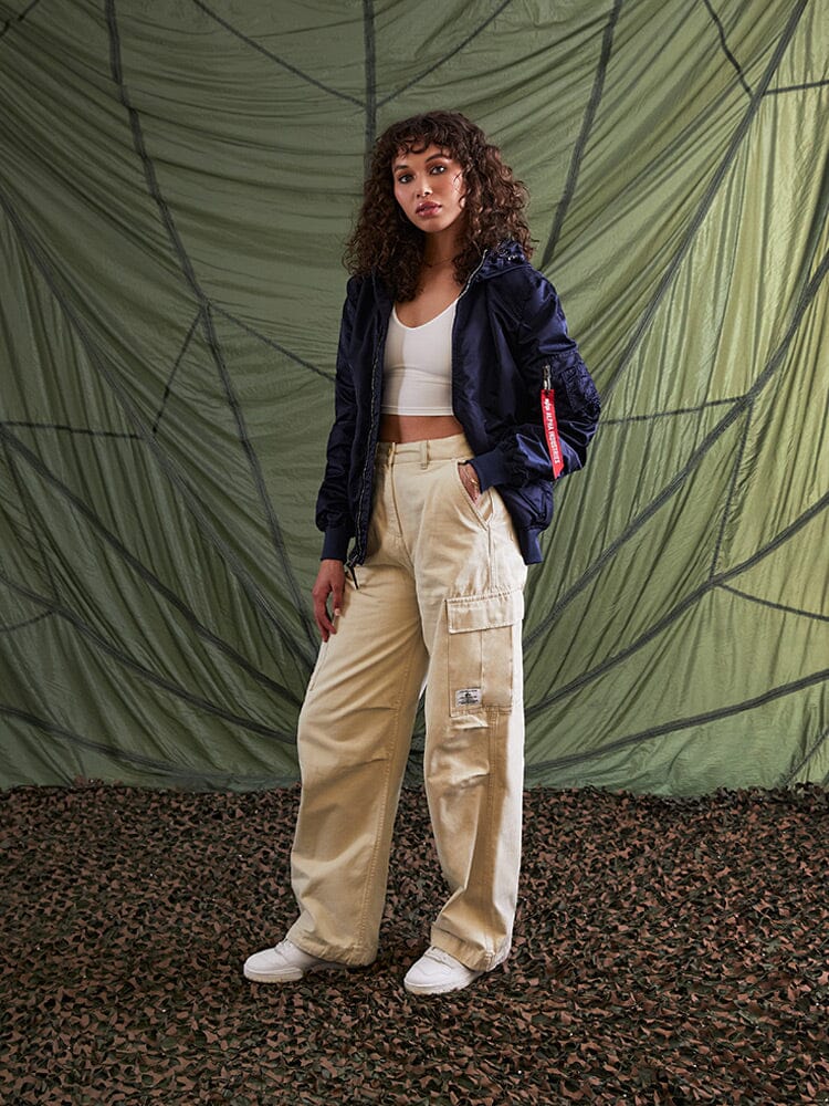A person wearing an Alpha Industries L-2B Hooded Gen II Bomber Jacket in Navy, a white top, beige cargo pants, and white sneakers.