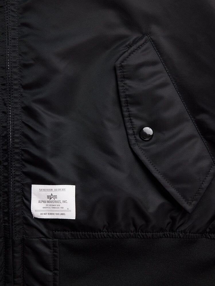 Close-up of the L-2B Hooded Gen II Bomber Jacket in Black by Alpha Industries, Inc., highlighting a side pocket with a button and a white label. This fashionable nylon jacket is also water-resistant, providing both style and practicality.