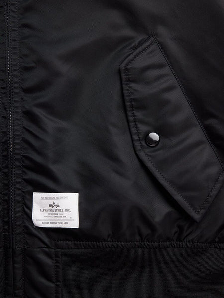 Close-up of the L-2B Hooded Gen II Bomber Jacket in black nylon, featuring a pocket with a button and an Alpha Industries, Inc. label stitched on the lower left side.