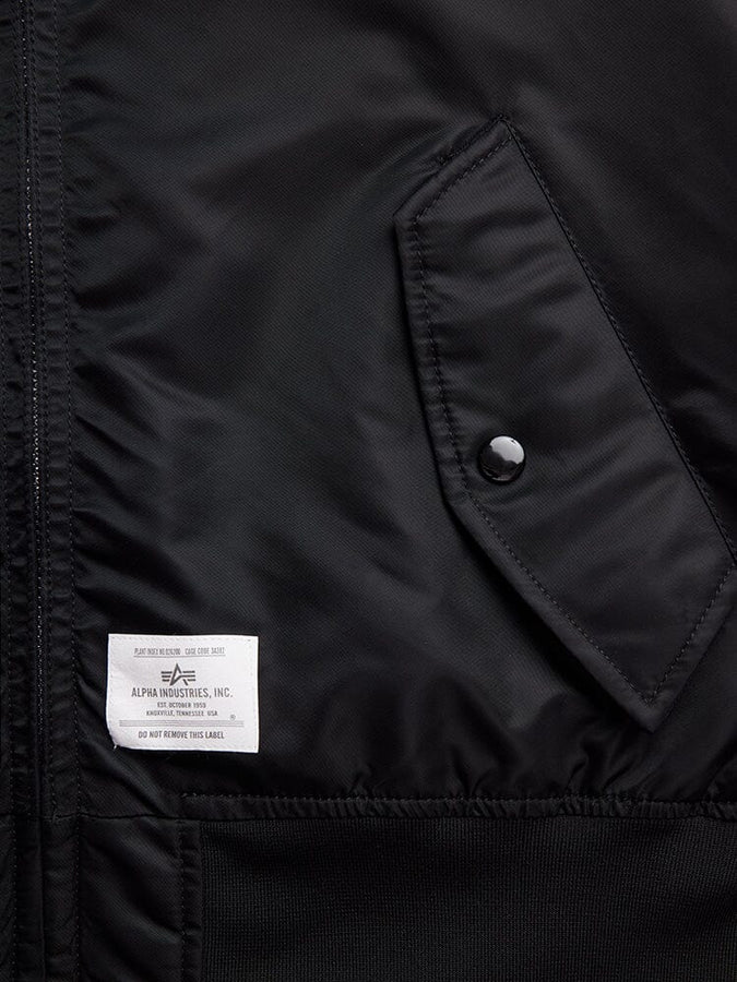 Close-up of the L-2B Hooded Gen II Bomber Jacket in black nylon, featuring a pocket with a button and an Alpha Industries, Inc. label stitched on the lower left side.