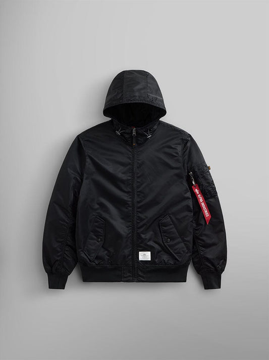 The L-2B Hooded Gen II Bomber Jacket by Alpha Industries, Inc. is a black nylon jacket featuring a hood, front zipper, two side pockets, and a distinctive red tag on the left sleeve. It is lightweight and water-resistant, making it ideal for different weather conditions.