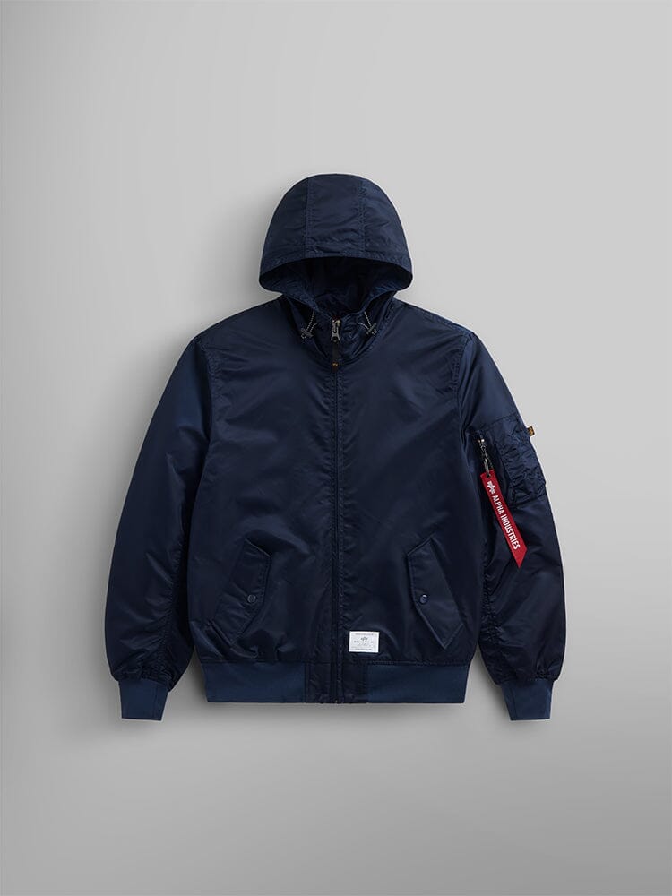 The L-2B Hooded Gen II Bomber Jacket by Alpha Industries, Inc., in Replica Blue, is a lightweight hooded jacket featuring a front zipper, two pockets, and a distinct red tag on the sleeve. Crafted from nylon, this flight jacket combines versatility with style.