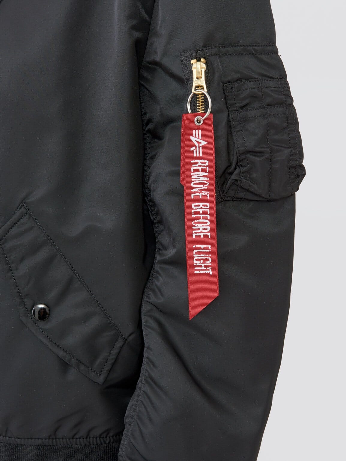 L-2B Natus W Bomber Jacket by Alpha Industries, black sleeve, zippered pocket, red REMOVE BEFORE FLIGHT tag, durable water resistant material.