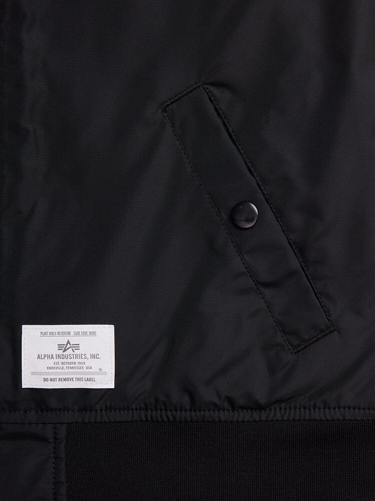 Close-up of a black fabric with a buttoned pocket and a white label reading Alpha Industries, Inc. The L-2B Skymaster Gen II Bomber Jacket W is made from lightweight nylon, offering water-resistant properties and featuring intricate oxygen tab details for enhanced functionality.