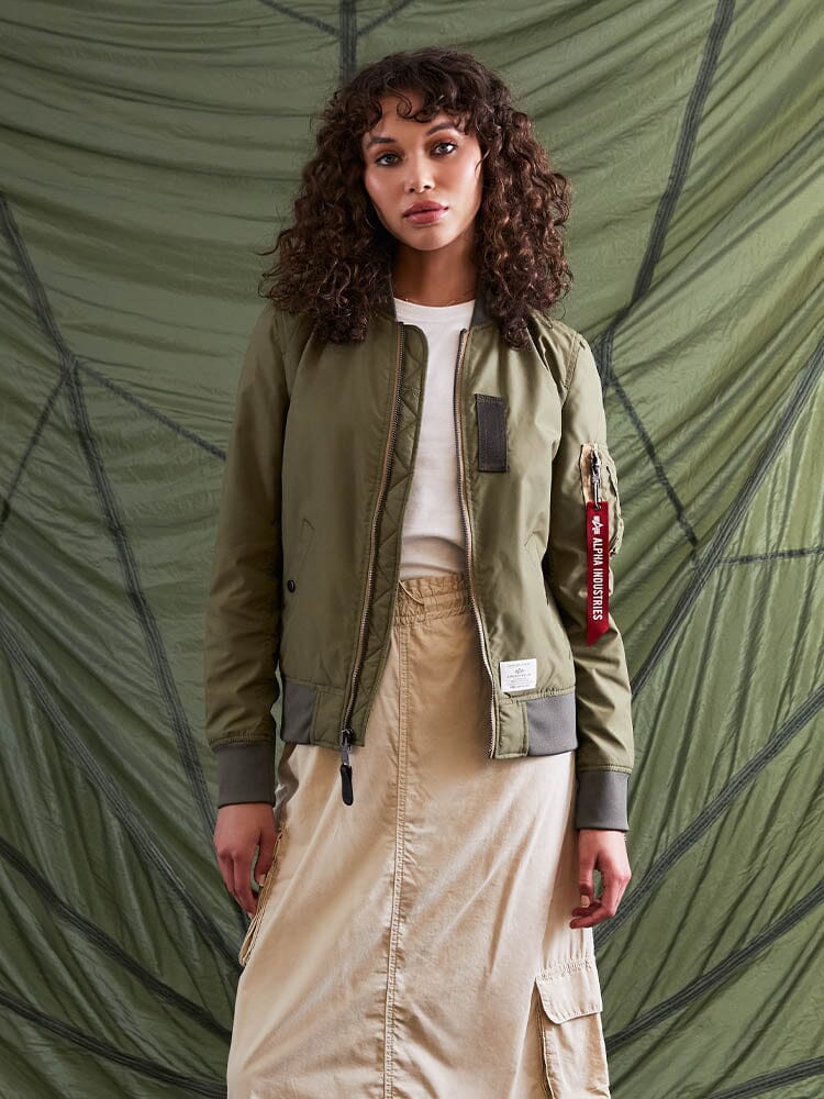 A person wearing the L-2B Skymaster Gen II Bomber Jacket by Alpha Industries, Inc. and a beige skirt stands.