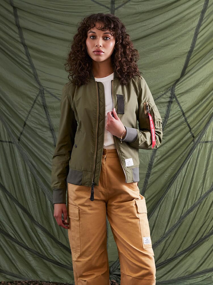A person wearing the Alpha Industries L-2B Skymaster Gen II Bomber Jacket in green, which is crafted from lightweight nylon and features water-resistant properties, along with tan cargo pants, highlighting subtle oxygen tab details.