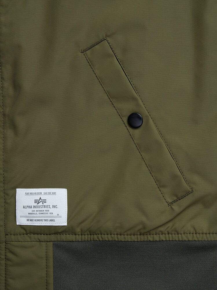 The close-up of the L-2B Skymaster Gen II Bomber Jacket W reveals a pocket with a black button, a white label from Alpha Industries, Inc., and intricate oxygen tab details.