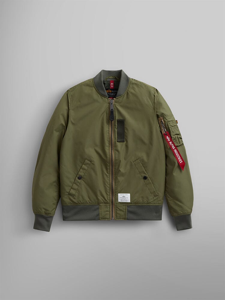 The L-2B Skymaster Gen II Bomber Jacket W by Alpha Industries is designed in OG-107 green and crafted from lightweight, water-resistant nylon. It features ribbed cuffs, hem, and collar, a zippered front closure, side pockets, and includes a stylish red oxygen tab detail on the sleeve.