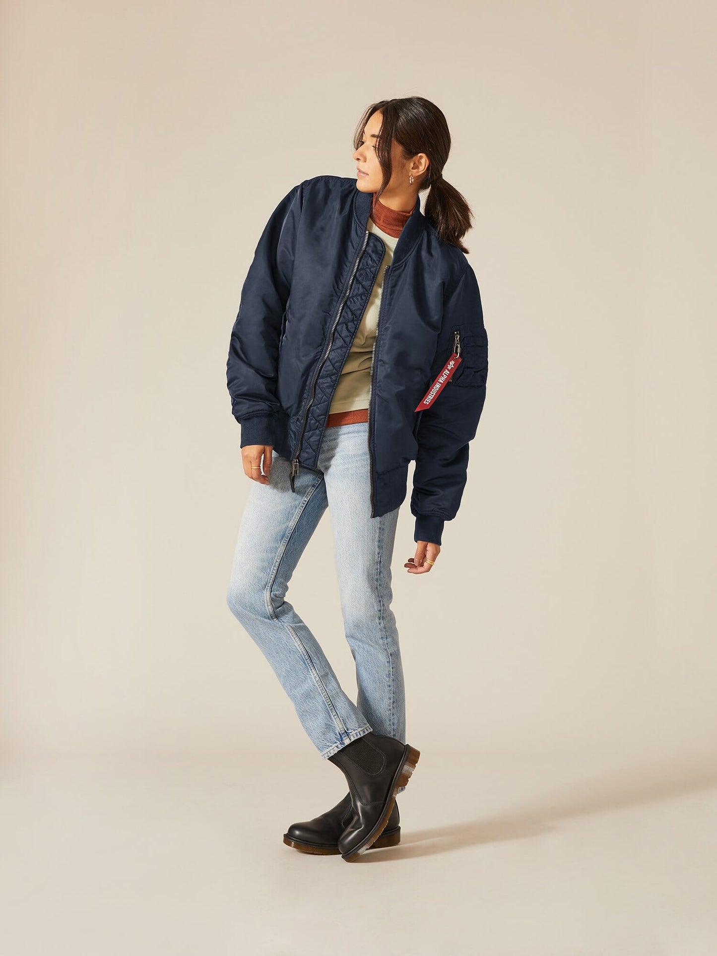 Clad in an Alpha Industries, Inc. MA-1 Battlewash Bomber Jacket, a beige sweater, and light jeans, a person balances on one leg.