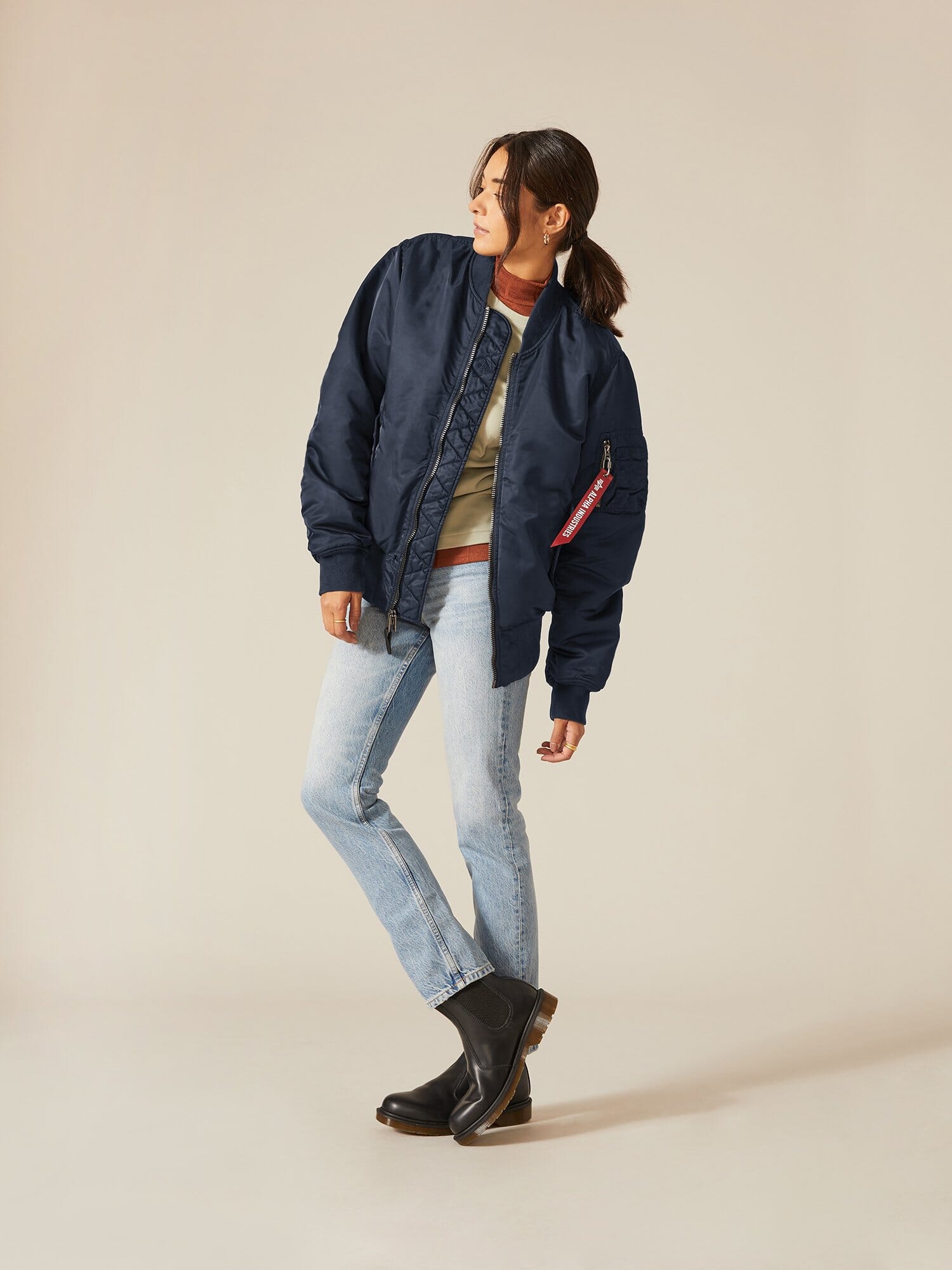 Clad in an Alpha Industries, Inc. MA-1 Battlewash Bomber Jacket, a beige sweater, and light jeans, a person balances on one leg.