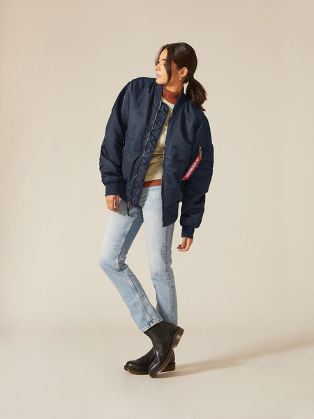 Clad in an Alpha Industries, Inc. MA-1 Battlewash Bomber Jacket, a beige sweater, and light jeans, a person balances on one leg.