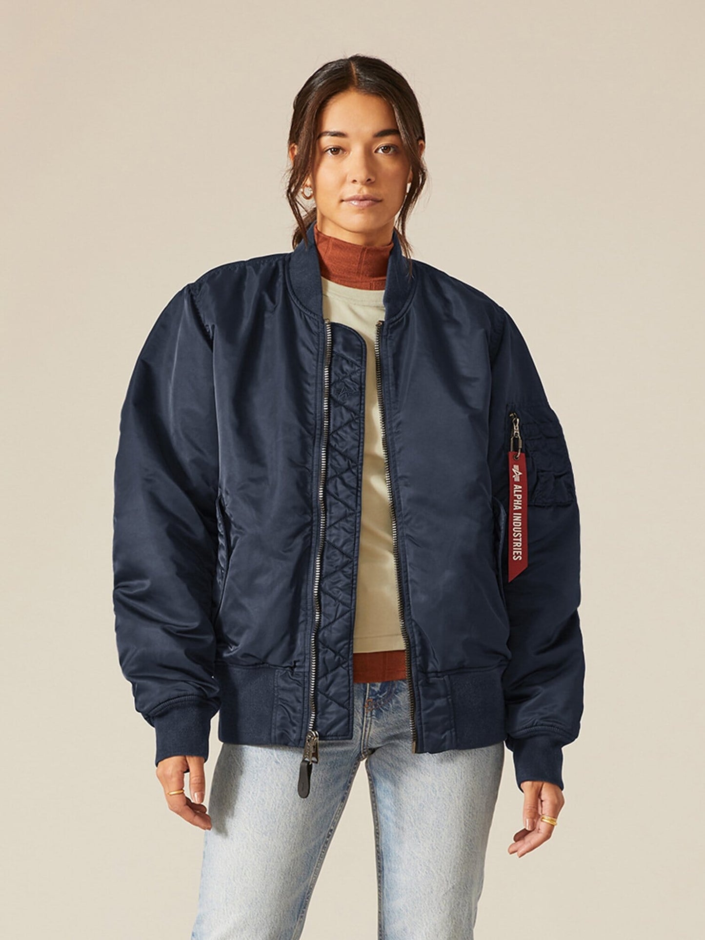 A person stands wearing a Dark Blue MA-1 Battlewash Bomber Jacket by Alpha Industries, Inc. over a brown turtleneck and light-colored jeans.