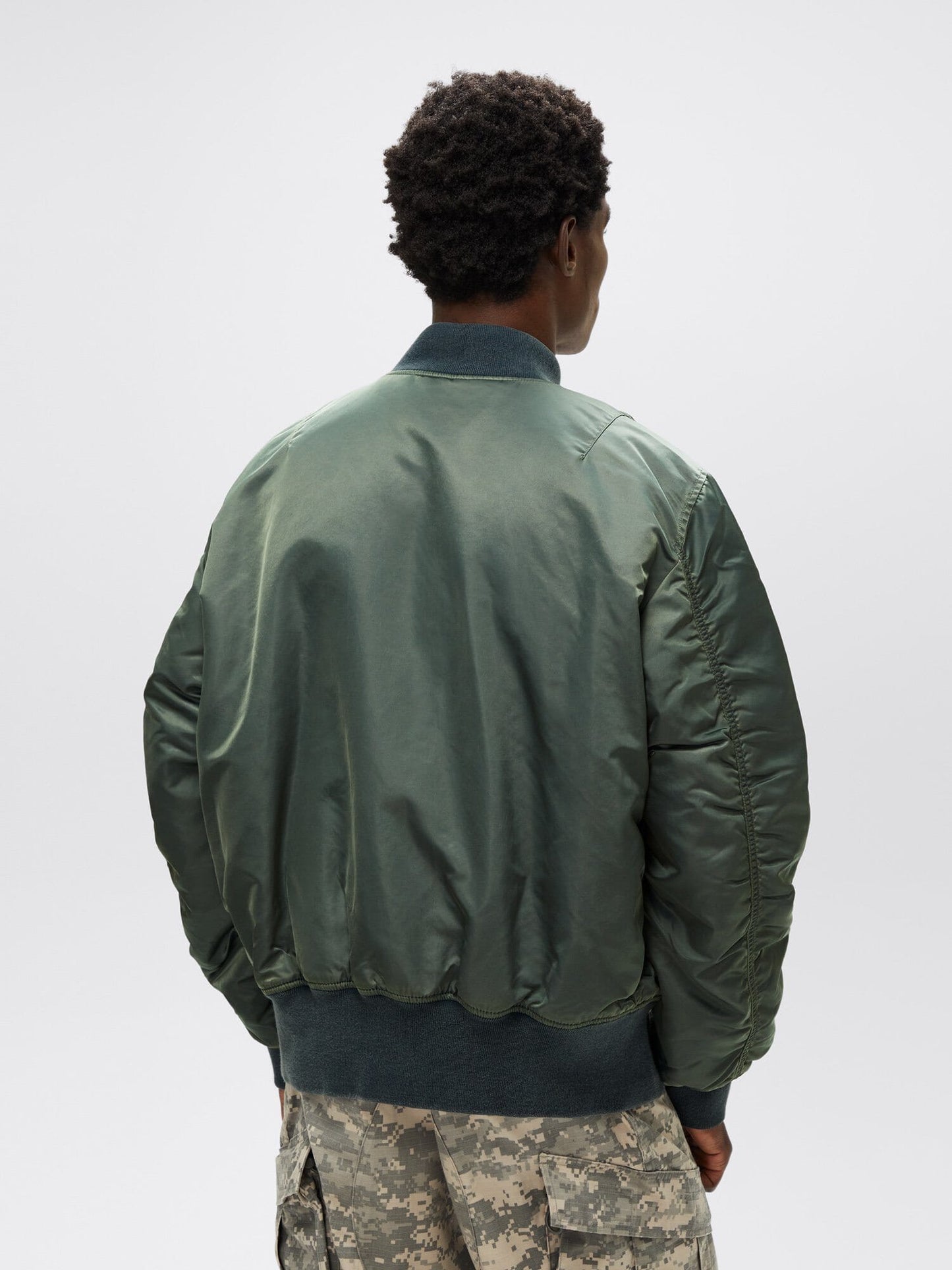 A person wearing an Alpha Industries MA-1 Battlewash Bomber Jacket in green and camouflage pants, facing away.