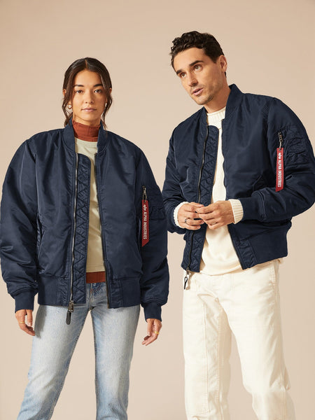Two individuals don matching navy MA-1 Battlewash Bomber Jackets from Alpha Industries, one pairing it with light jeans and a beige sweater, the other with blue jeans and a t-shirt.