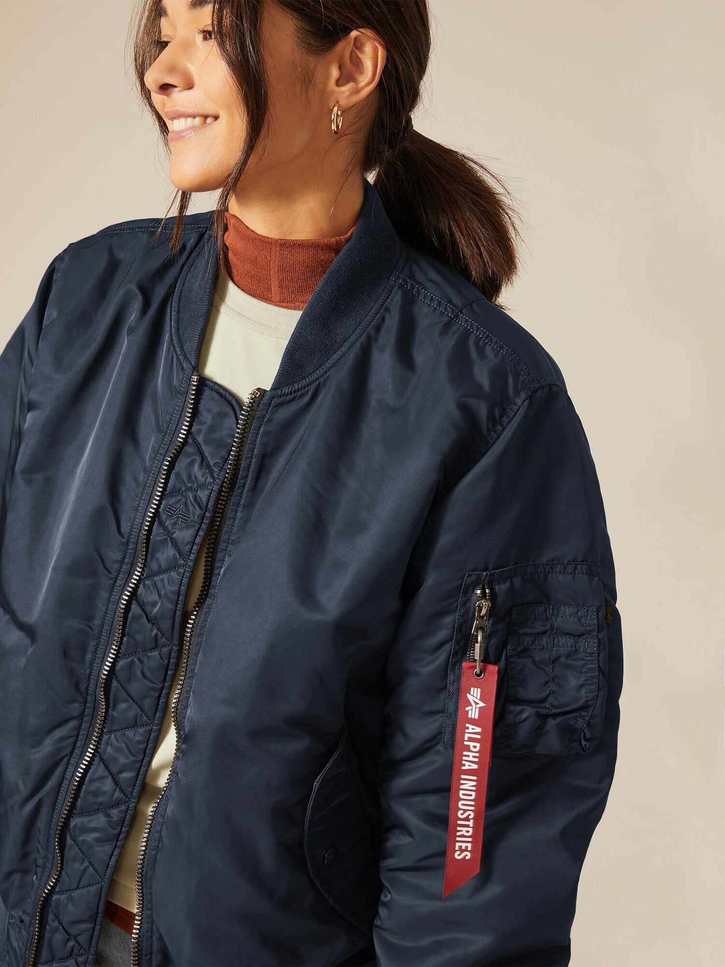 Someone is wearing a navy MA-1 Battlewash Bomber Jacket, featuring the recognizable Alpha Industries, Inc. tag on the arm. This timeless piece, celebrated for its versatility, presents a sleek look that perfectly aligns with its status as an essential reversible jacket.