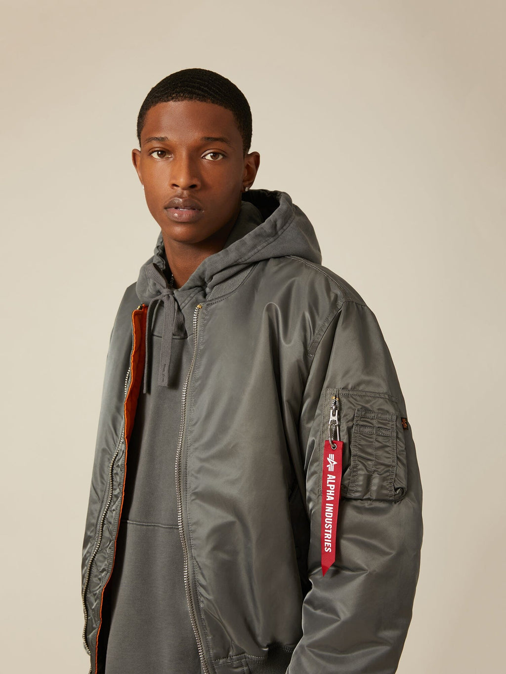 Grey MA-1 Bomber Jacket by Alpha Industries with red tag and grey hoodie.