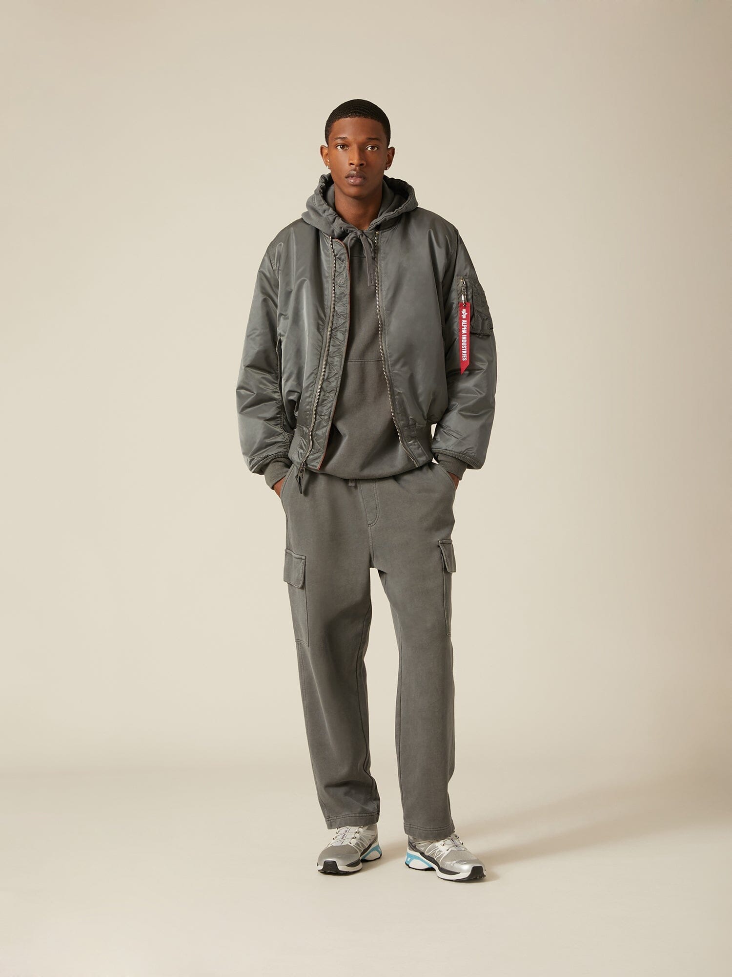 Alpha Industries MA-1 bomber jacket in gray flight nylon with ribbed cuffs and hem, gray hoodie, cargo pants, and sneakers.