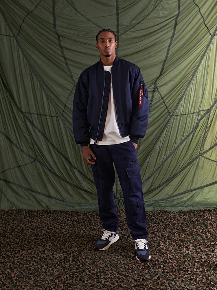 Alpha Industries MA-1 Bomber Jacket in navy flight nylon with white t-shirt, navy cargo pants, and navy sneakers.