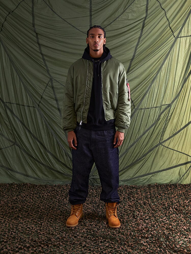 Olive Alpha Industries MA-1 Bomber Jacket, black hoodie, dark jeans, tan boots.
