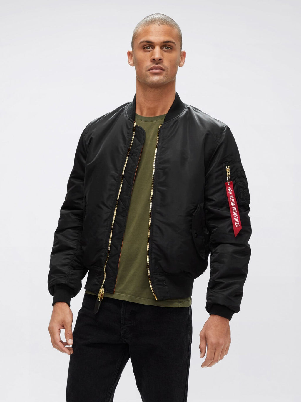 Front view of black Alpha Industries MA-1 Bomber Jacket Slim Fit showing gold zipper, ribbed cuffs, and sleeve pocket with red tag.