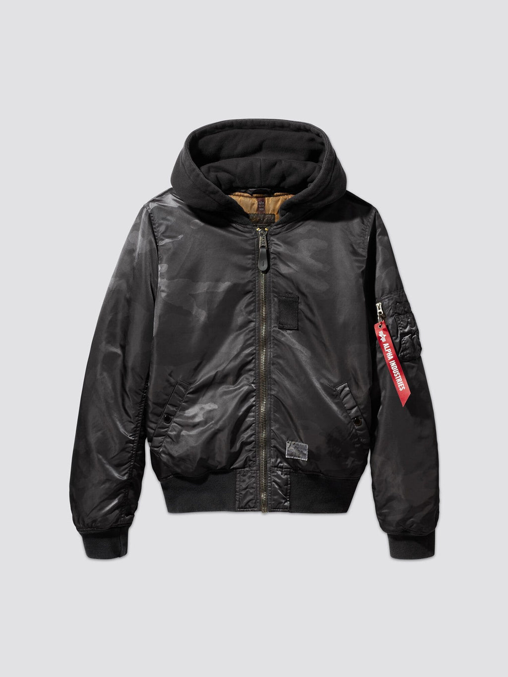 Alpha Industries, Inc.'s MA-1 Hooded Battlewash Bomber Jacket features a front zipper and a distinctive red tag on the sleeve. This design closely follows the iconic MA-1 flight jacket style, offering both warmth and timeless fashion appeal.