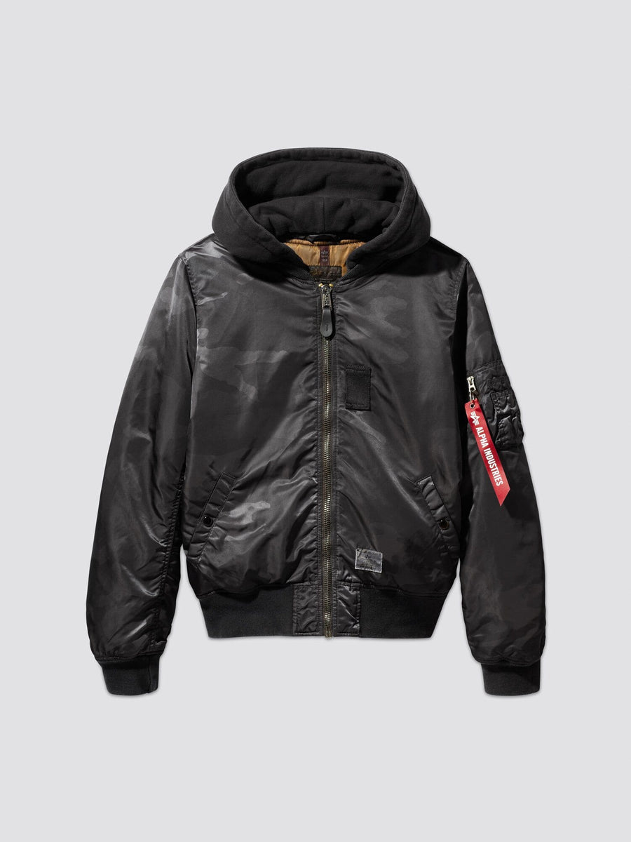 Alpha Industries, Inc.'s MA-1 Hooded Battlewash Bomber Jacket features a front zipper and a distinctive red tag on the sleeve. This design closely follows the iconic MA-1 flight jacket style, offering both warmth and timeless fashion appeal.