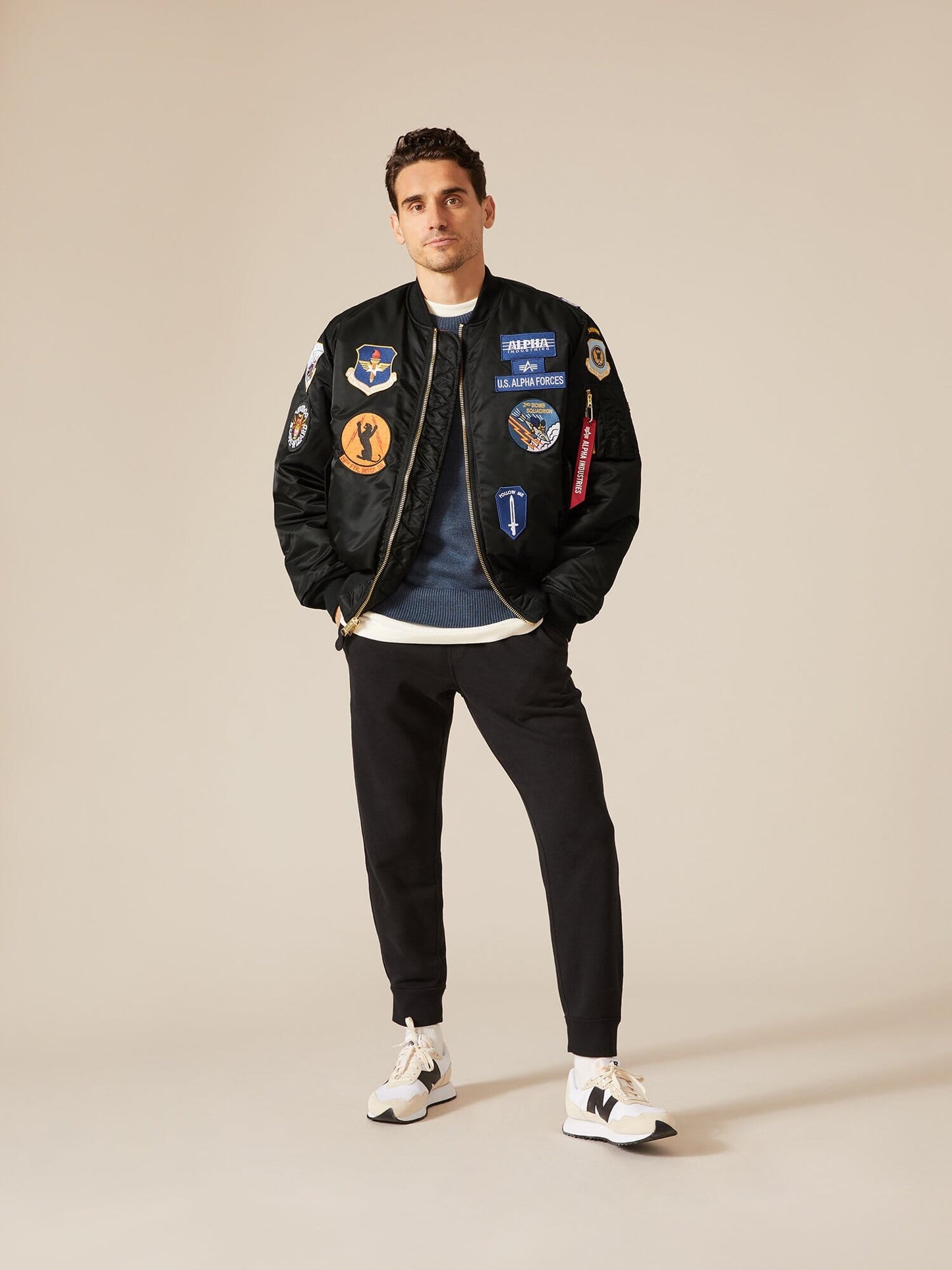 Alpha Industries MA-1 Squadron Bomber Jacket in black with colorful patches, blue shirt, black pants, and white sneakers.