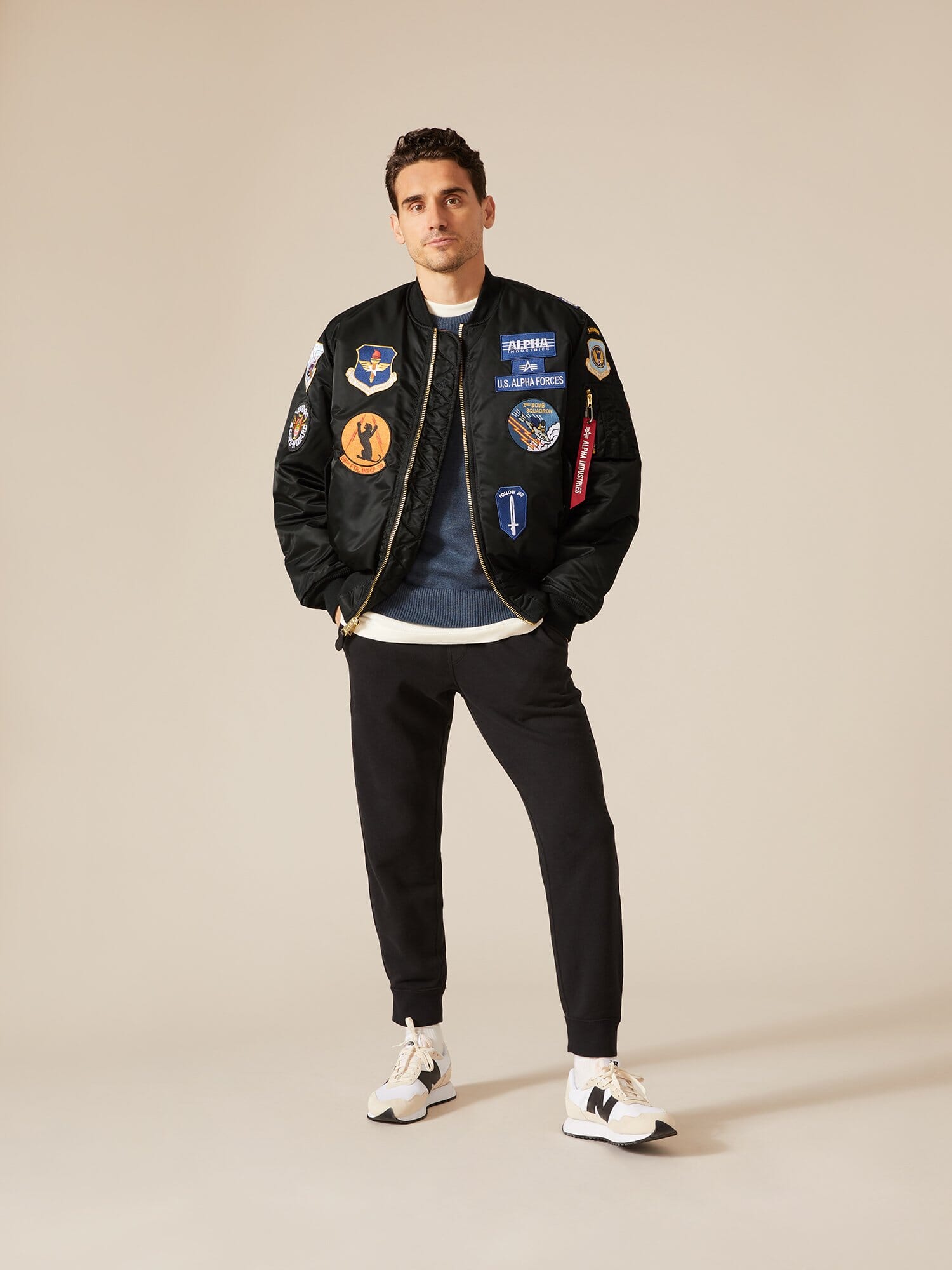 Alpha Industries MA-1 Squadron Bomber Jacket in black with colorful patches, blue shirt, black pants, and white sneakers.