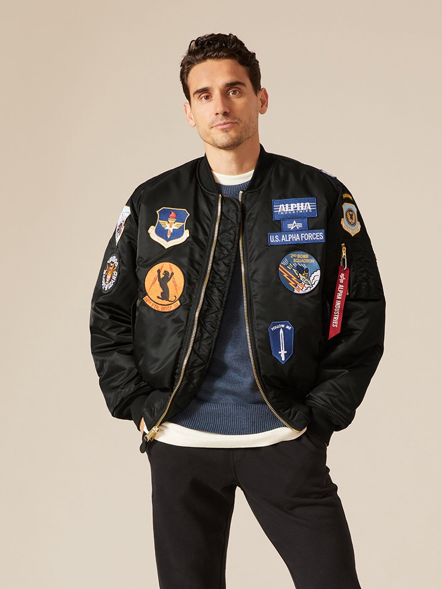 Alpha Industries MA-1 Squadron Bomber Jacket with colorful squadron patches, blue sweater, and black pants.