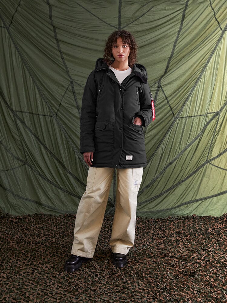 A person wearing the N-3B Altitude Mod Parka W by Alpha Industries, Inc., with its US Navy-inspired design featuring a water-resistant snorkel hood, and beige pants.