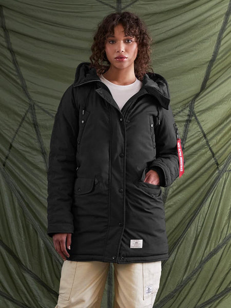 A person wearing the N-3B Altitude Mod Parka W by Alpha Industries, Inc., a US Navy-inspired black parka with a snorkel hood, paired with light-colored pants.