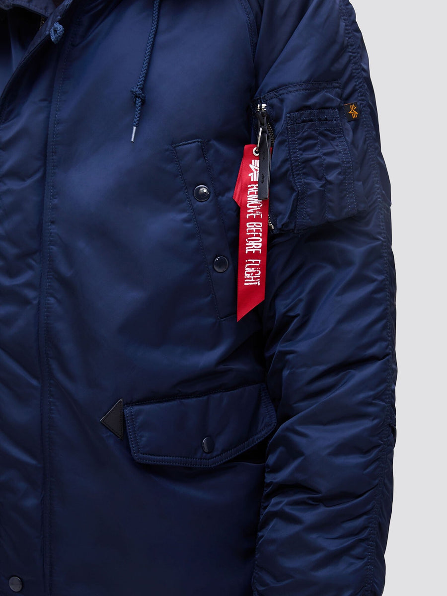Alpha Industries N-3b Slim Gen I Parka in navy with zippered sleeve pocket, snap buttons, MA-1 utility pocket, and red Remove Before Flight tag. Water resistant.