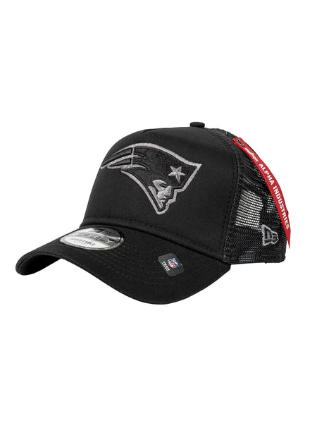 The New England Patriots x Alpha x New Era 940 Cap by Alpha Industries features a stylized face logo on the front, mesh back panels for breathability, and a distinctive red tag on the side, all in black.