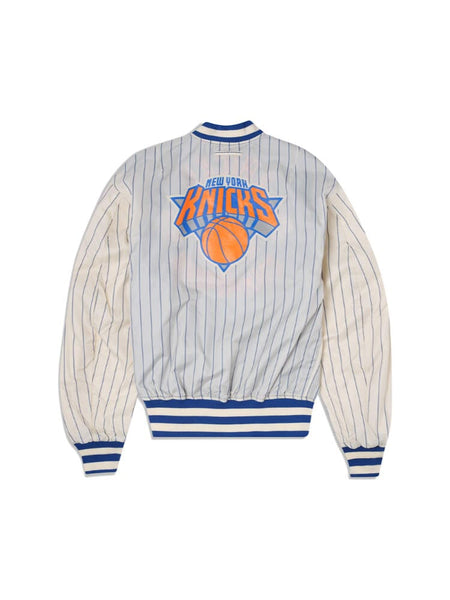 The New York Knicks x Alpha x New Era L-2B Bomber Jacket by Alpha Industries is a blue and white striped bomber jacket with the New York Knicks logo on the back, adorned with team patches.