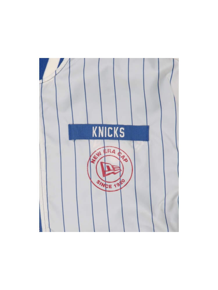 Close-up of a blue and white striped garment featuring the Knicks text and a distinctive red circular logo labeled New Era Cap Since 1920, reminiscent of the New York Knicks X Alpha X New Era L-2B Bomber Jacket from Alpha Industries.