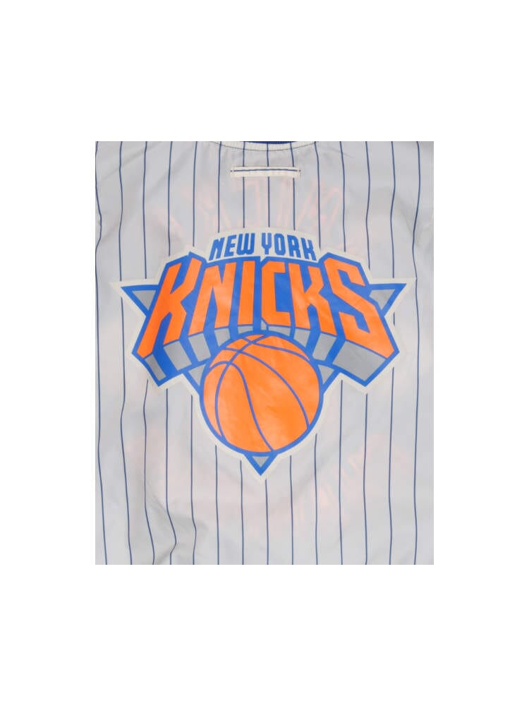 A vibrant plastic bag, reminiscent of the bold designs from Alpha Industries and New Era, showcases the New York Knicks logo alongside blue vertical stripes and a striking basketball graphic.